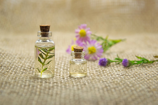 Essential oils in transparent glass bottles alongside flower and leaves