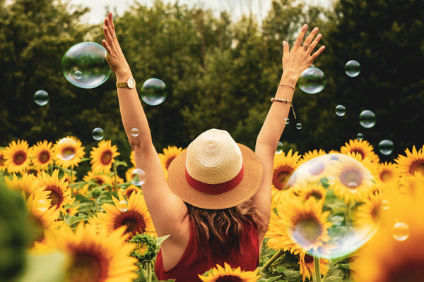 A happy, care-free woman raising her hands in a field of yellow sunflowers and bubbles