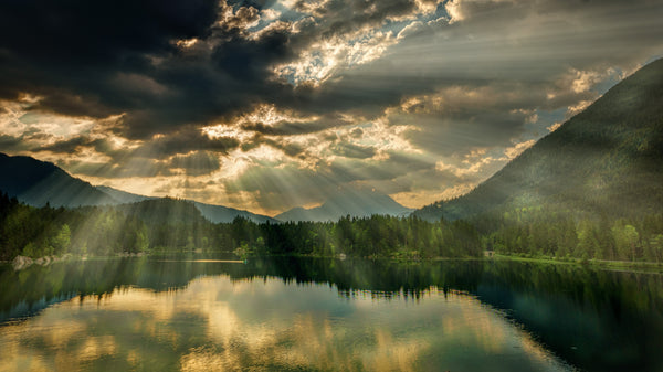 Sun shining upon the calming still water surrounded by green mountains