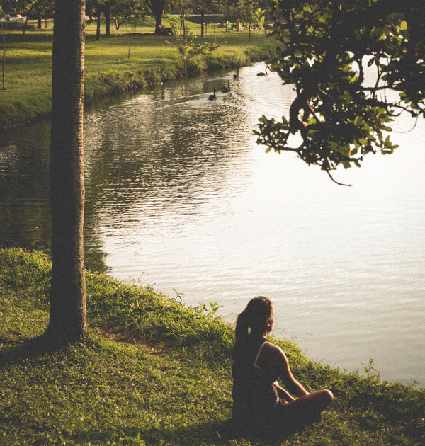 Woman meditating by the peaceful still lake surrounded by green grass and trees